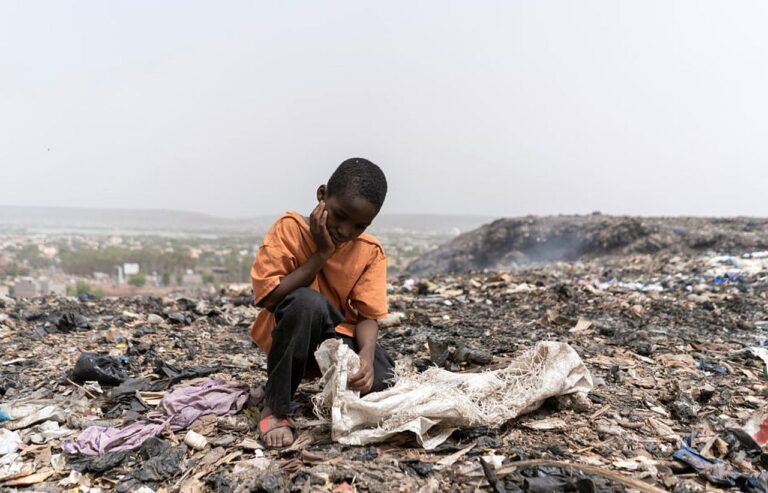 Miserable hungry African slum child looking for edible and recyclable items in a huge urban garbage dump