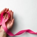 Woman holding pink ribbon on white background, top view with space for text. Breast cancer awareness concept