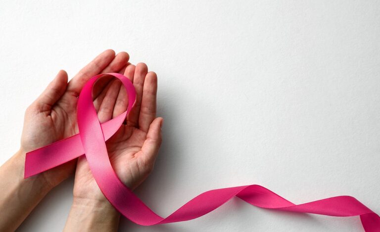 Woman holding pink ribbon on white background, top view with space for text. Breast cancer awareness concept